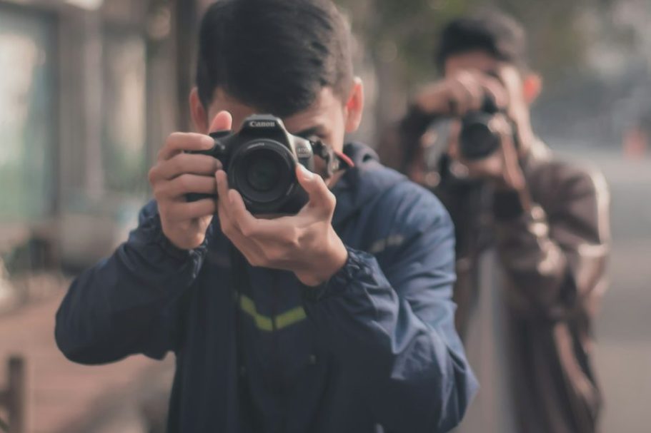 La Formazione Due persone che scattano foto in una strada urbana, con alberi sullo sfondo.