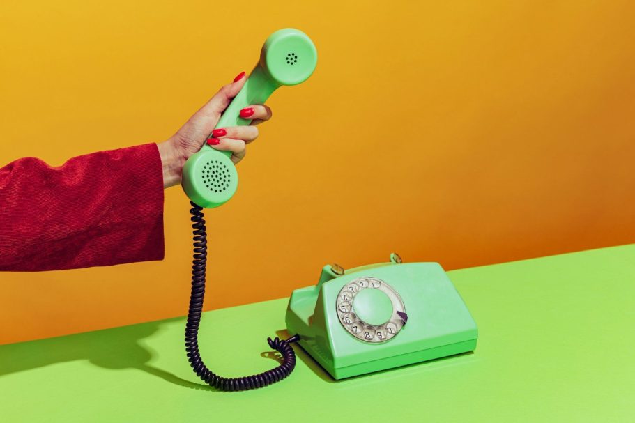 Contatti Mano che tiene un telefono verde su sfondo arancione e superficie verde.